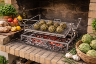 Parrilla giratoria de acero inoxidable para barbacoa cocinando alcachofas sobre brasas.