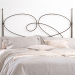 Cabecero de forja Aina para cama matrimonial con diseño curvo decorativo en hierro y ropa de cama en tonos neutros