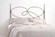 Cabecero de forja Aina para cama matrimonial con diseño curvo decorativo en hierro y ropa de cama en tonos neutros